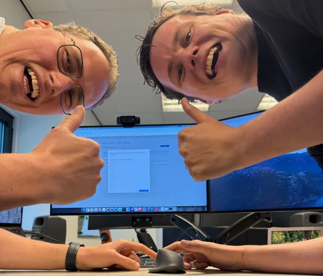 Ton and Mick give a thumbs up, laughing, as they press the button together to release the app.