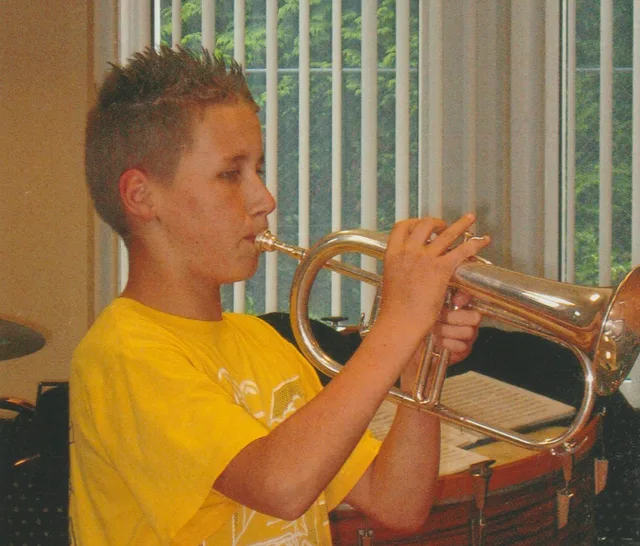 Young Ton in a yellow T-shirt plays the flugelhorn at rehearsal, with a bass drum behind him.